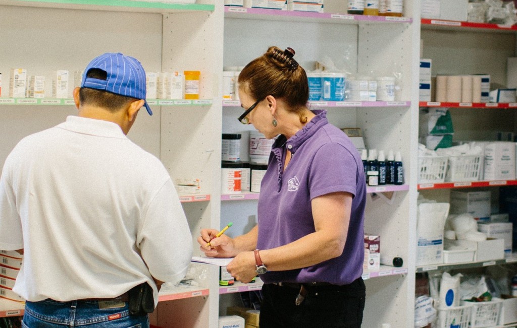 a person writing on a clipboard next to a person in a pharmacy
